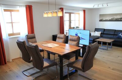 Wohn- und Essbereich Künstlhäusl Moderner Wohn- und Essbereich mit Holztisch, Polsterstühlen, dunklem Sofa und Fernseher.
