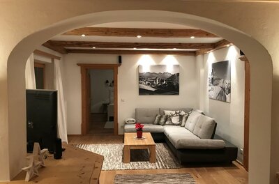 Wohnzimmer Apartment Hahnenkammblick Modernes Wohnzimmer mit Ecksofa, Holztisch und Deckenbalken unter einem Rundbogen.