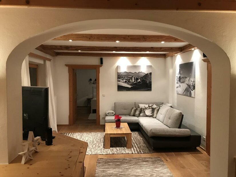 Wohnzimmer Apartment Hahnenkammblick Modernes Wohnzimmer mit Ecksofa, Holztisch und Deckenbalken unter einem Rundbogen.