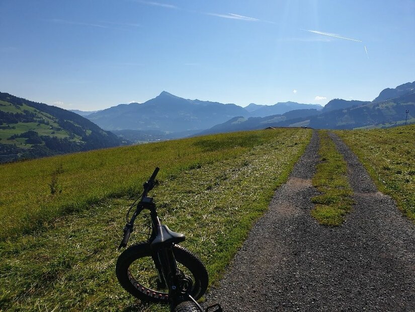 Mountainbike am Obergaisberg Ein Mountainbike steht auf einer Almwiese neben einem Schotterweg mit Blick auf die Berge.