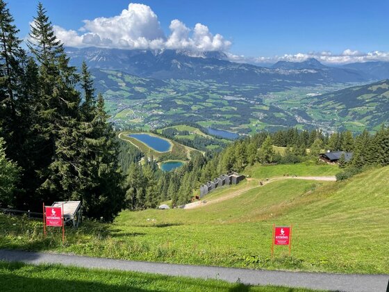 Blick auf die Streif Blick von einem Grashang auf Bergseen und ein bewaldetes Tal vor einem Gebirgsmassiv unter Wolken.