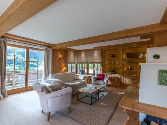 Wohnbereich im Haus Schmidt Wohnzimmer mit hellen Polstermöbeln, Holzwänden, Einbauregalen und Blick durch eine Glastür auf die Berge.