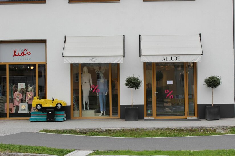 Allude Ladengeschäft Außenansicht des Bekleidungsgeschäfts Allude mit Schaufenstern, Markisen und einem gelben Kinder-Spielauto.