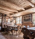 Rustikale Gaststube aus hellem Holz mit Holztischen, Stühlen mit Herz-Ausschnitt und Geweih-Leuchtern.
