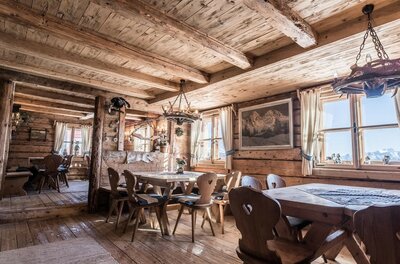 Gaststube Berggasthaus Resterhöhe Rustikale Gaststube aus hellem Holz mit Holztischen, Stühlen mit Herz-Ausschnitt und Geweih-Leuchtern.