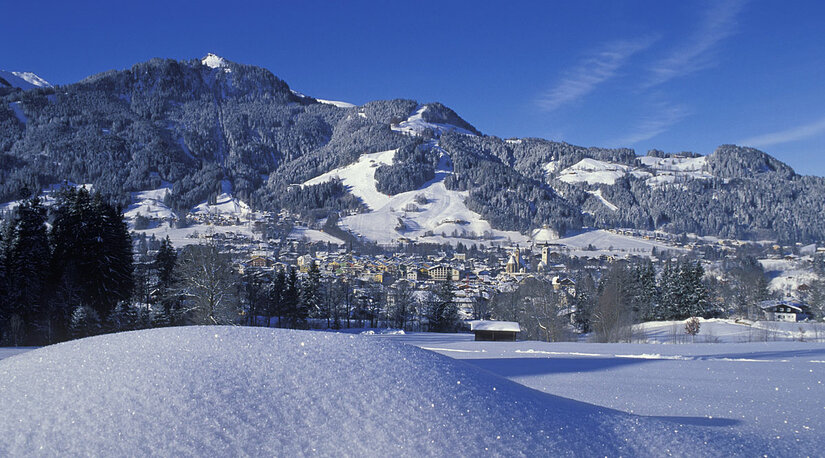 Winteransicht von Kitzbühel Verschneite Berglandschaft mit Blick auf Kitzbühel unter blauem Himmel.
