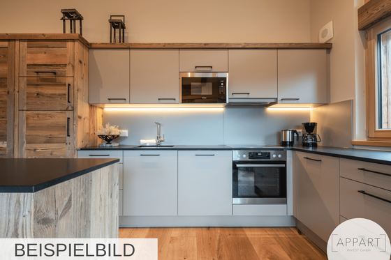 Küche Alpin Residenzen Eichenheim Moderne Küchenzeile mit hellgrauen Fronten, Holzschränken und integrierten Elektrogeräten.