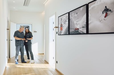 Univ.- Prfo. Dr. Rainer Hahn Ein heller Flur mit modernem Design. Zwei Personen stehen nebeneinander und betrachten Bilder an der Wand.