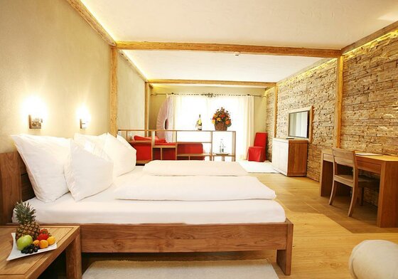 Zimmer in Rosi's Sonnbergstuben Modernes Hotelzimmer mit Doppelbett aus Holz, Steinwand und Schreibtisch.