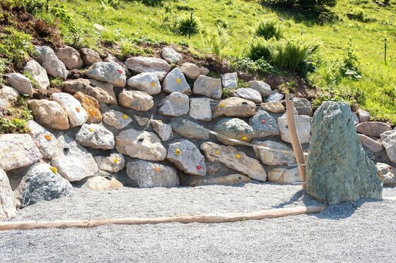 Boulderwand Sommererlebnis Streif Künstliche Boulderwand aus Natursteinen mit bunten Klettergriffen auf einem Kiesplatz.