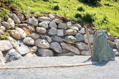 Boulderwand Sommererlebnis Streif Künstliche Boulderwand aus Natursteinen mit bunten Klettergriffen auf einem Kiesplatz.