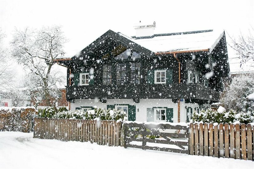 Weberhaus im Winter Verschneites zweistöckiges Holzhaus mit weißer Fassade und dunklem Balkon bei Schneefall.