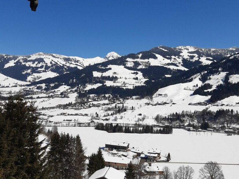Winterpanorama am Bärenbichl Verschneite Gebirgslandschaft mit bewaldeten Hängen und kleinen Siedlungen unter blauem Himmel.