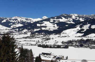 Winterpanorama am Bärenbichl Verschneite Gebirgslandschaft mit bewaldeten Hängen und kleinen Siedlungen unter blauem Himmel.