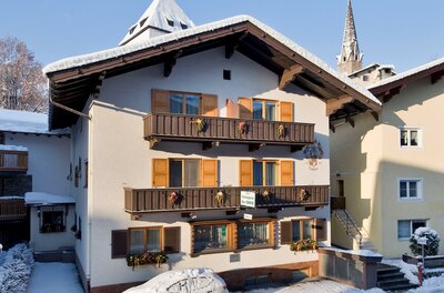 Alpines Gästehaus mit Holzbalkonen und schneebedecktem Dach im Winter.
