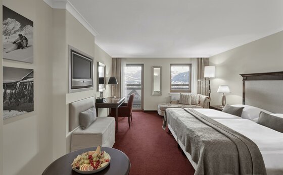 Lebenberg Schlosshotel Classic Zimmer Modernes Hotelzimmer mit Doppelbett, rotem Teppichboden, Schreibtisch und Blick auf die Berge.