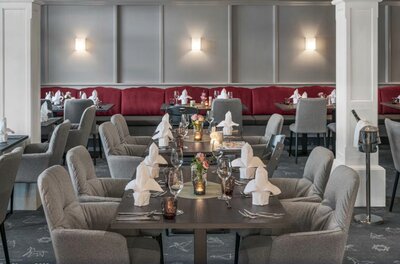 Restaurant im Lisi Family Hotel Eingedeckte Tische in einem Restaurant mit grauen Polstersesseln und roter Sitzbank.