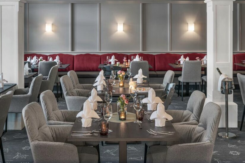 Restaurant im Lisi Family Hotel Eingedeckte Tische in einem Restaurant mit grauen Polstersesseln und roter Sitzbank.