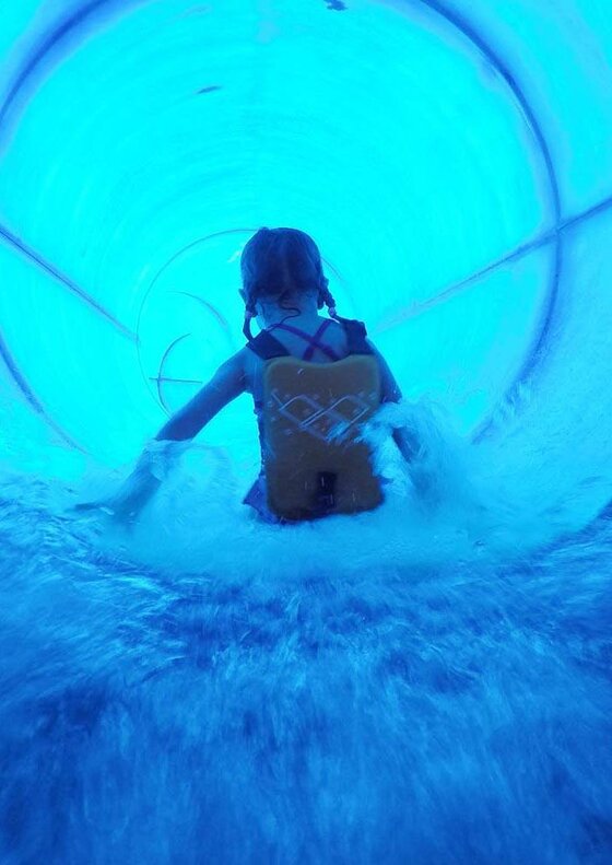 Rutsche Ein Kind rutscht mit einem Schwimmhilfe durch eine bunte Wasserrutsche. Das Wasser spritzt während des Rutsches aus der Rutsche.