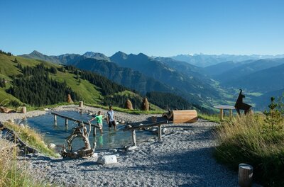 Kneippanlage an der Bichlalm Zwei Personen in einem Kneippbecken auf einem Bergplateau vor einem weiten Gebirgspanorama.