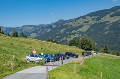 Wanderparkplatz Schering Parkende Autos am Rand einer asphaltierten Bergstraße vor bewaldeten Hängen.