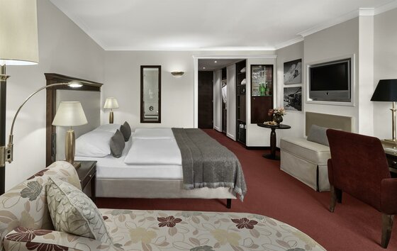 Lebenberg Schlosshotel Classic Zimmer Modernes Hotelzimmer mit Doppelbett, rotem Teppichboden, Sitzecke und Fernseher.