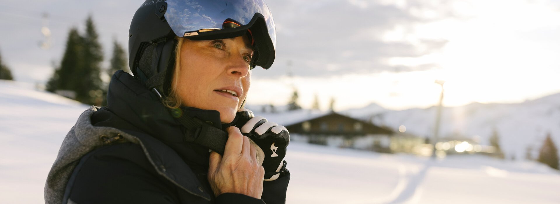 A mature lady in ski gear adjusts her helmet in a winter landscape