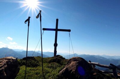 Gipfelkreuz bei der Bichlalm Gipfelkreuz und Wanderstöcke vor Gebirgspanorama bei Sonnenschein.