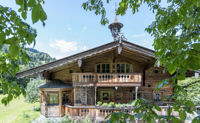 Apartment Nussbaum Traditionelles Holzhaus mit Balkonen und Glockenturm hinter grünen Blättern.