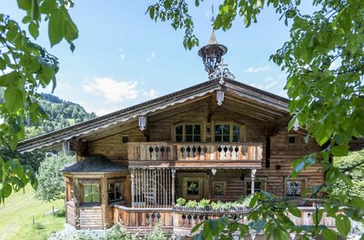Apartment Nussbaum Traditionelles Holzhaus mit Balkonen und Glockenturm hinter grünen Blättern.