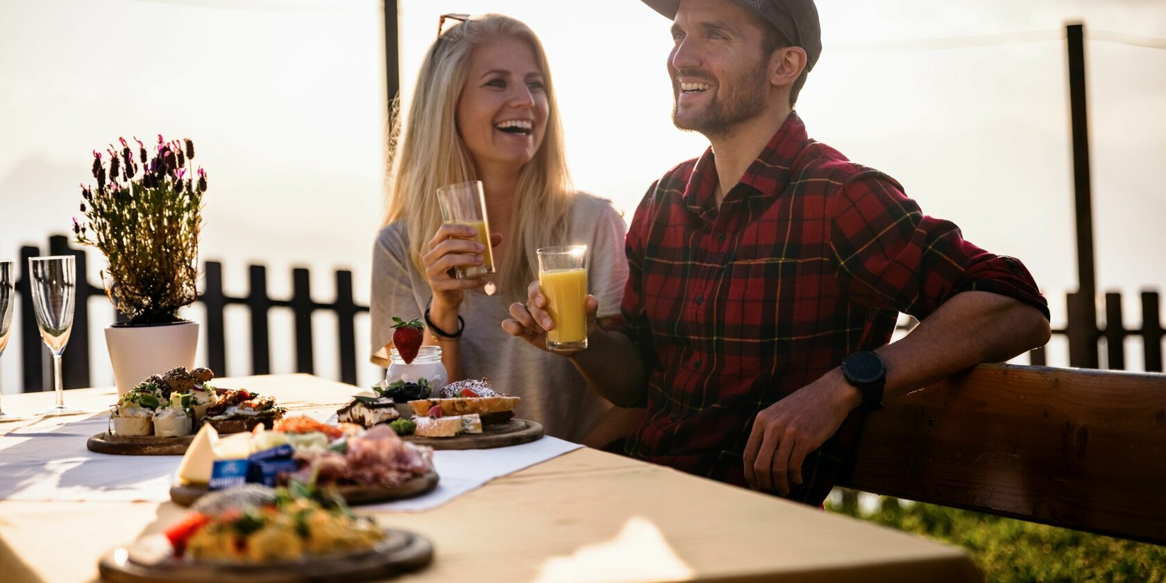 Ein fröhliches Paar genießt ein Frühstück im Freien, umgeben von köstlichen Speisen und einer malerischen Aussicht.