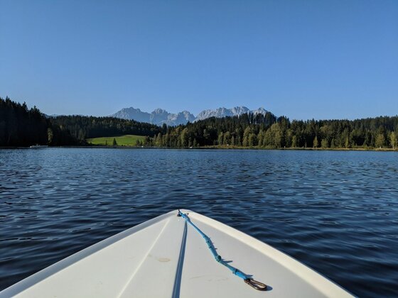 Bootsfahrt auf dem Schwarzsee Blick vom Bug eines Bootes über einen See auf einen Wald und ein Gebirgsmassiv unter blauem Himmel.