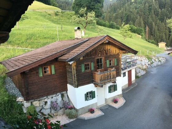 Traditionelles Holzhaus mit weißem Sockel an einem asphaltierten Weg vor grünen Almwiesen.