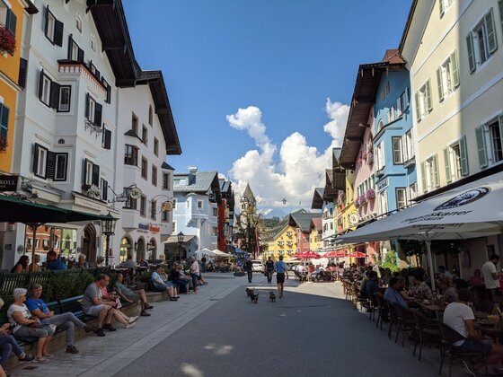 Fußgängerzone Kitzbühel Fußgängerzone in Kitzbühel mit farbigen Häuserfassaden und Außengastronomie unter blauem Himmel.