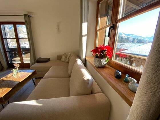Wohnzimmer mit beigem Sofa, Holztisch und Fenster mit Blick auf verschneite Berge.