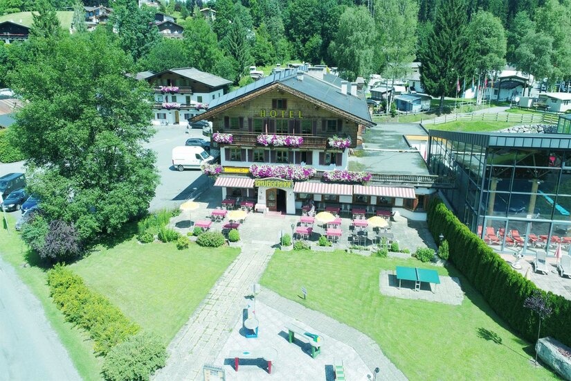 Bruggerhof mit Greißler Ein malerisches Hotel umgeben von grünen Bäumen und bunten Blumen. Terassen mit Tischen und Stühlen laden zum Entspannen ein.