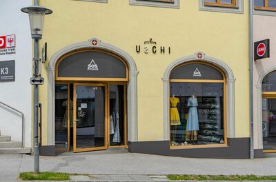 Außenansicht des Modegeschäfts Uschi mit zwei Rundbogenfenstern und gelber Fassade.
