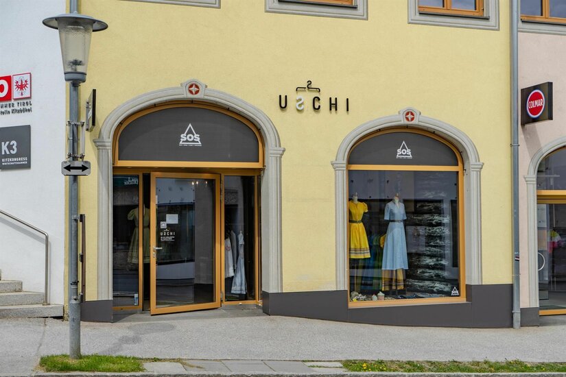 Modegeschäft Uschi Außenansicht des Modegeschäfts Uschi mit zwei Rundbogenfenstern und gelber Fassade.