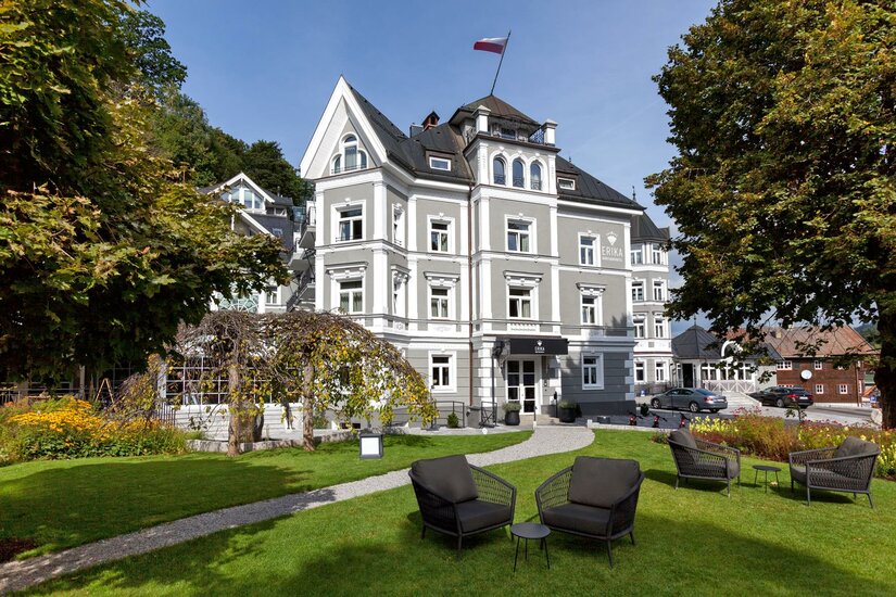ERIKA Boutiquehotel Kitzbühel Mehrstöckiges graues Boutiquehotel mit weißer Fassadengliederung und Gartenanlage.