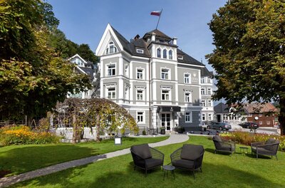 ERIKA Boutiquehotel Kitzbühel Mehrstöckiges graues Boutiquehotel mit weißer Fassadengliederung und Gartenanlage.