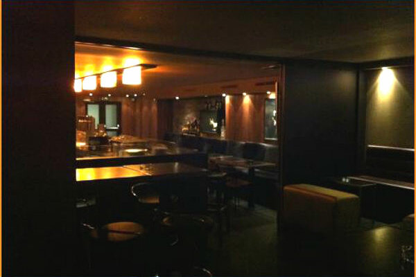 Innenansicht einer dunkel gestalteten Bar mit Holzelementen und gedimmter Beleuchtung.