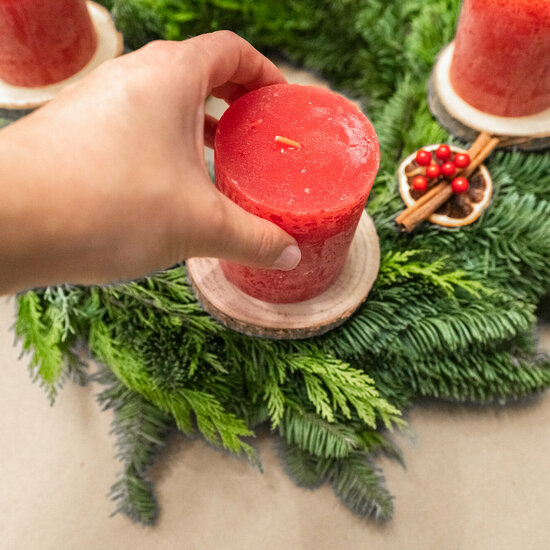 A hand places a red candle on wooden discs on an Advent wreath