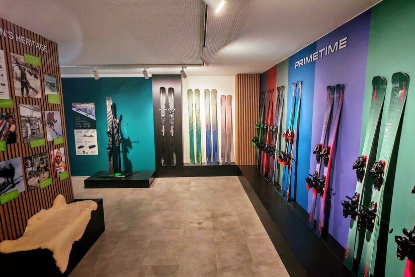 Ein moderner Ausstellungsraum mit verschiedenen Skiern an der Wand. Die Wände sind bunt gestaltet und es gibt Informationsmaterial über die Produkte.