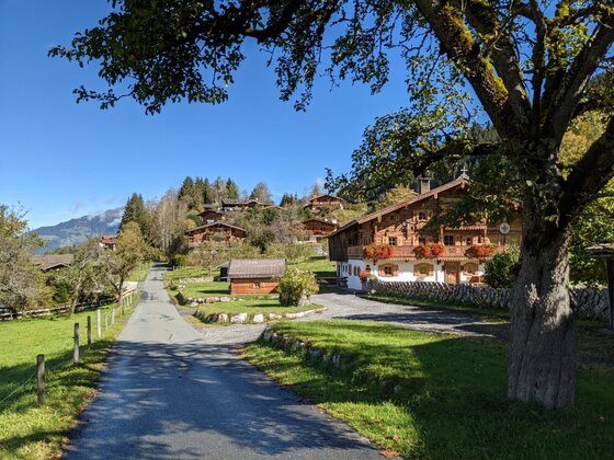 Museumsweg Jochberg Asphaltierter Weg führt an traditionellen Holzhäusern mit Blumenschmuck in Jochberg vorbei.