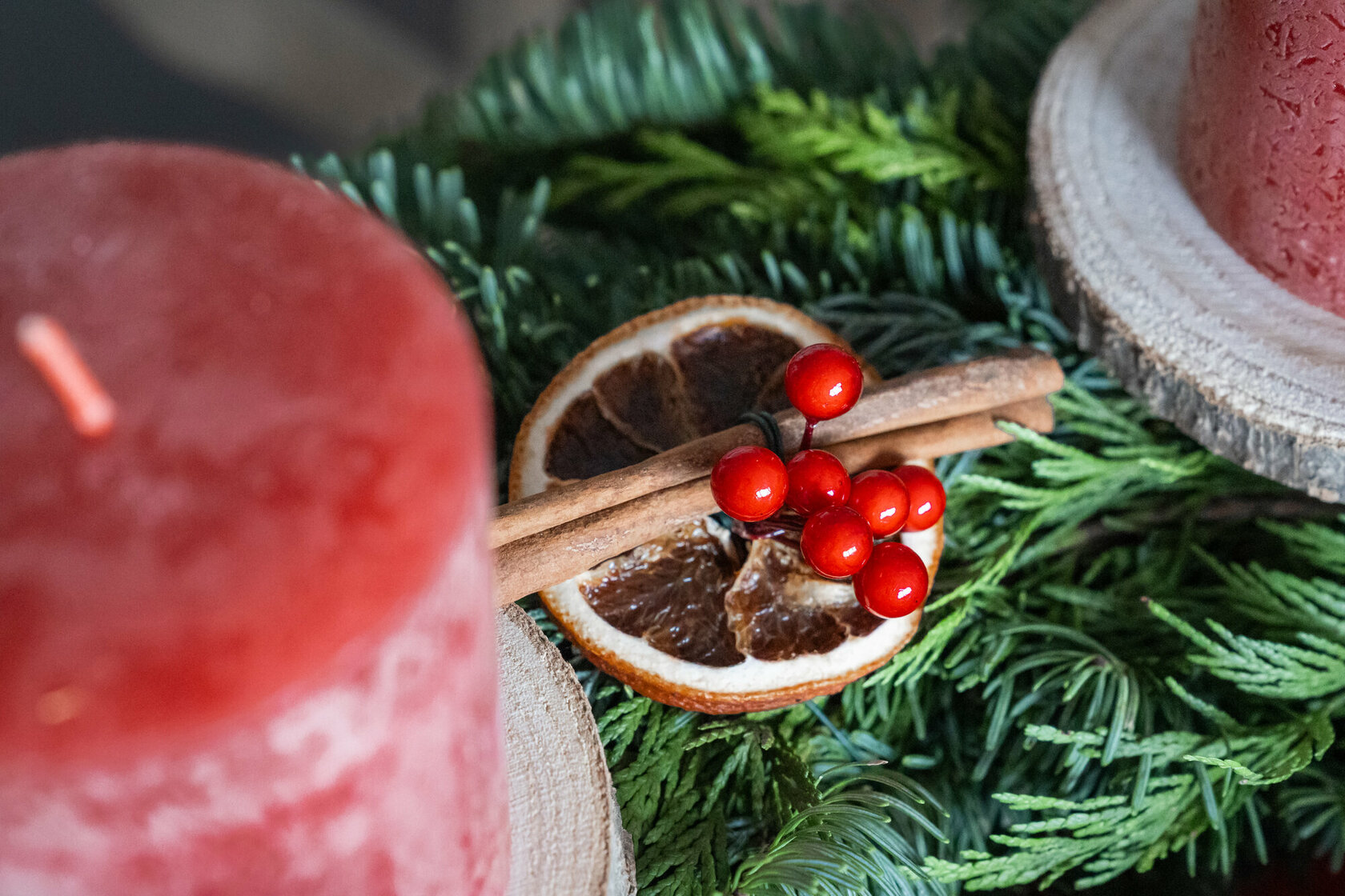 A dried orange slice, a cinnamon stick and two red candles on a bed of twigs