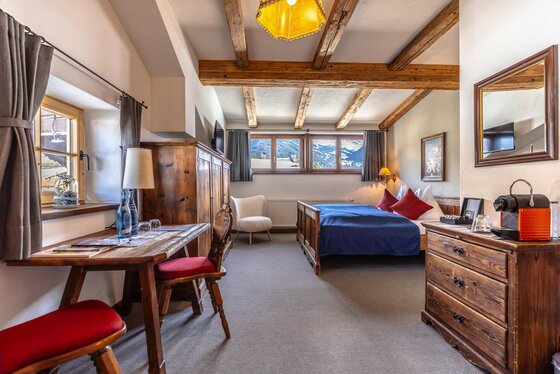 Zimmer im Gasthof Auwirt Rustikales Hotelzimmer mit Holzmöbeln, Doppelbett, Holzbalkendecke und Fenster mit Bergblick.