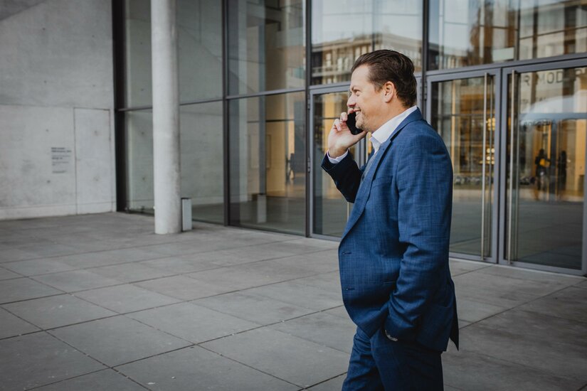 Egger und Graf <p>Ein geschäftlich gekleideter Mann telefoniert lächelnd vor einem modernen Gebäude.</p>