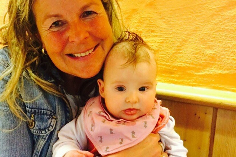 Eine lächelnde Frau hält ein Baby in den Armen. Der Hintergrund ist orangefarben, was eine freundliche Atmosphäre schafft.