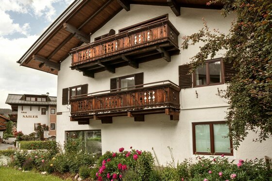 Appartement Elisabeth Kitzbühel Alpines Wohnhaus mit weißen Wänden, zwei Holzbalkonen und Blumenbeeten im Vordergrund.