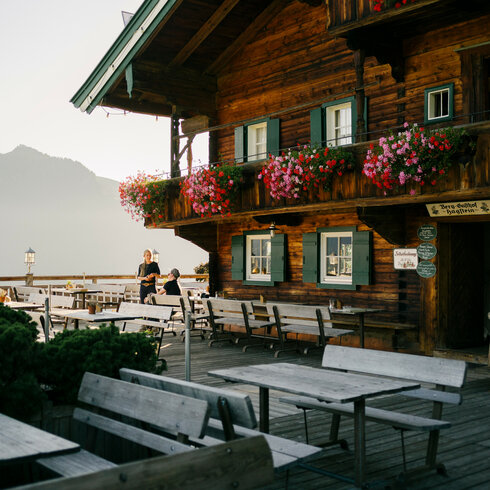 Eine rustikale Berghütte mit blühenden Balkonblumen und einer einladenden Terrasse, die einen atemberaubenden Blick auf die Berge bietet.